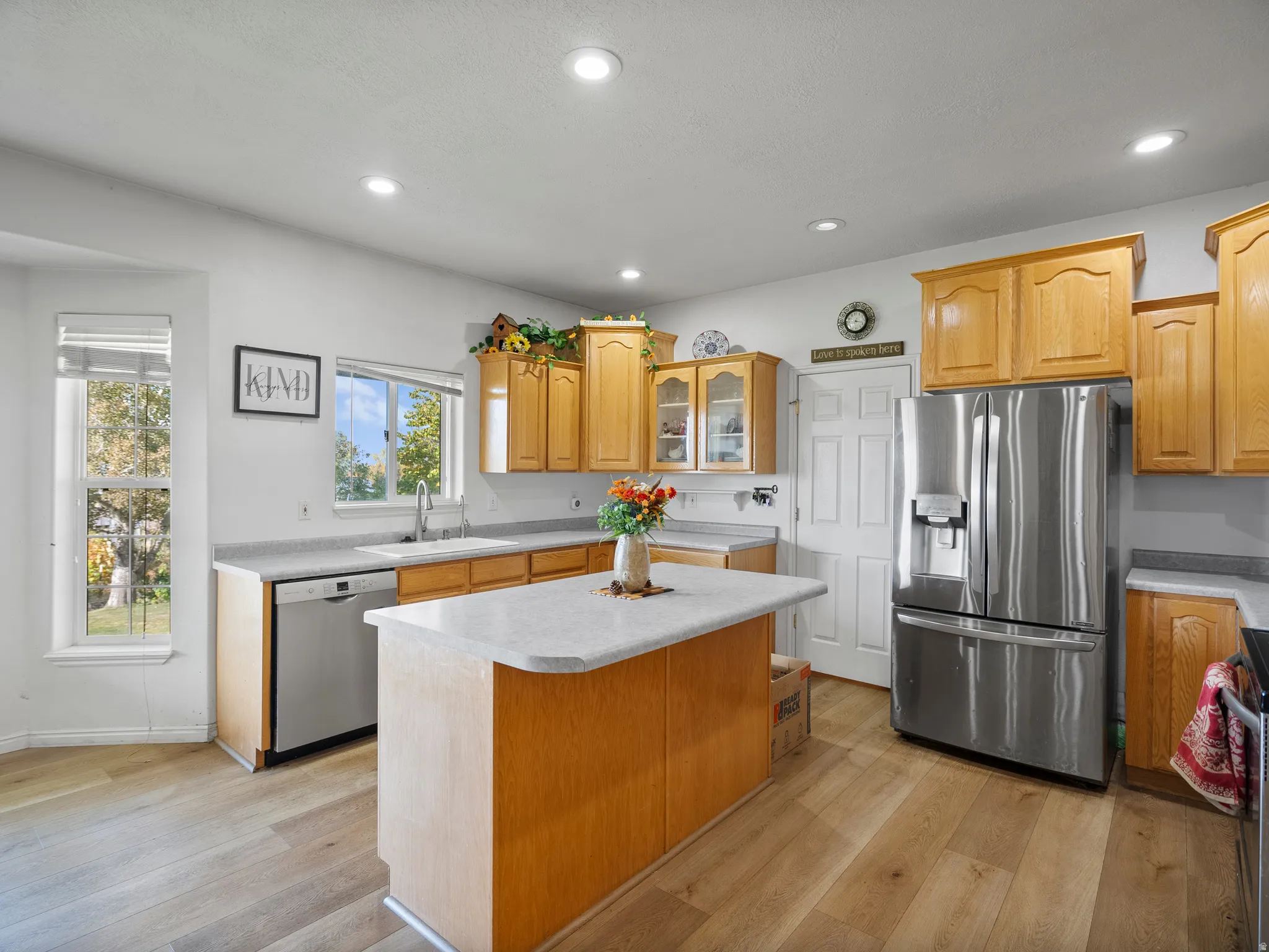 Kitchen with glass fronted cabinets, stainless steel appliances, light wood-style floors, a center island, and recessed lighting