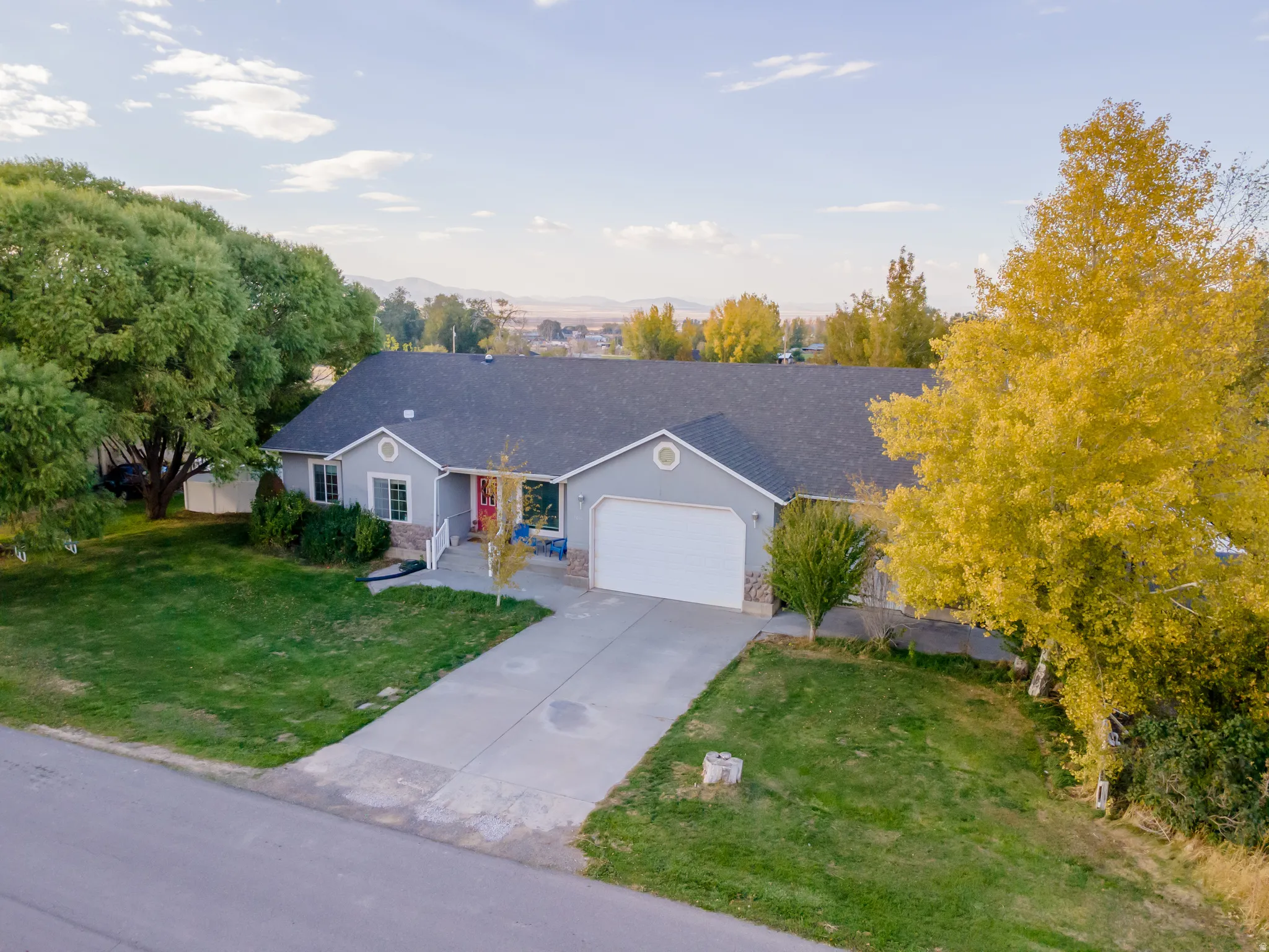 Single story home featuring a front yard, a garage, driveway, a shingled roof, and stucco siding