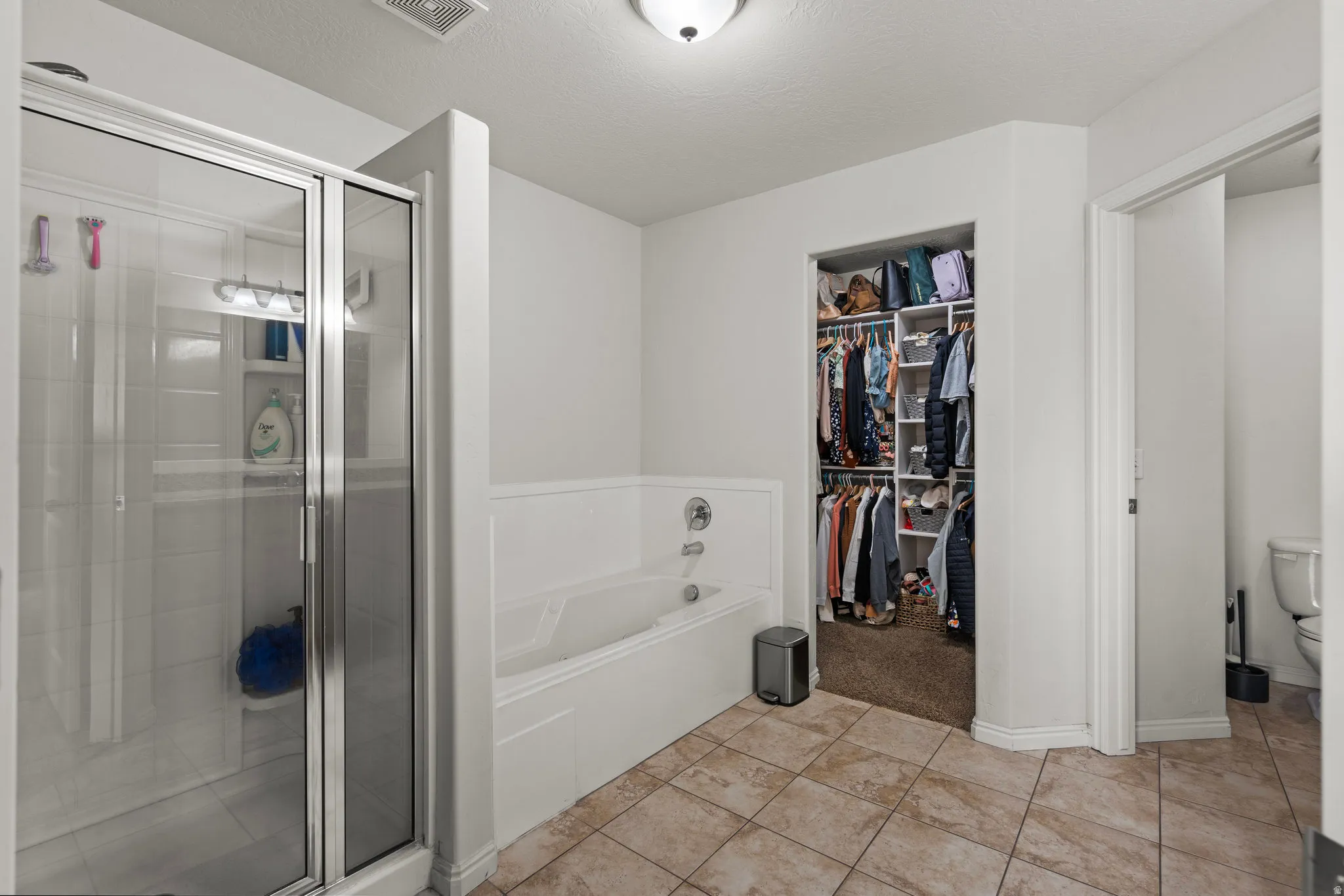 Full bath featuring a bath, a shower stall, a spacious closet, light tile patterned floors, and a textured ceiling
