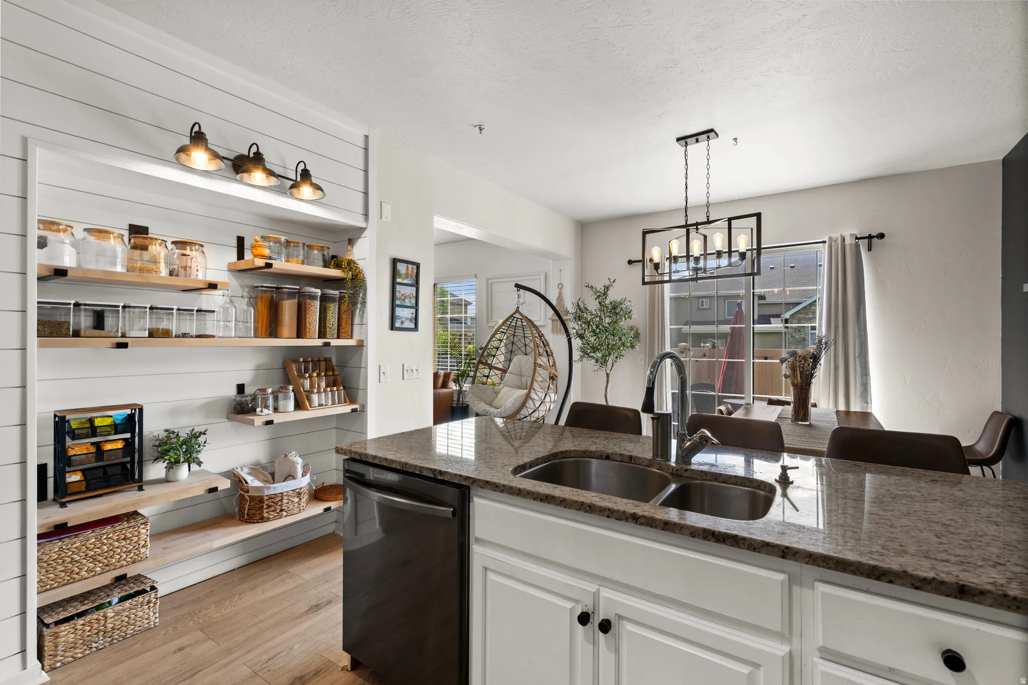 Kitchen with white cabinetry, dishwasher, dark stone counters, light wood-type flooring, and suspended lighting