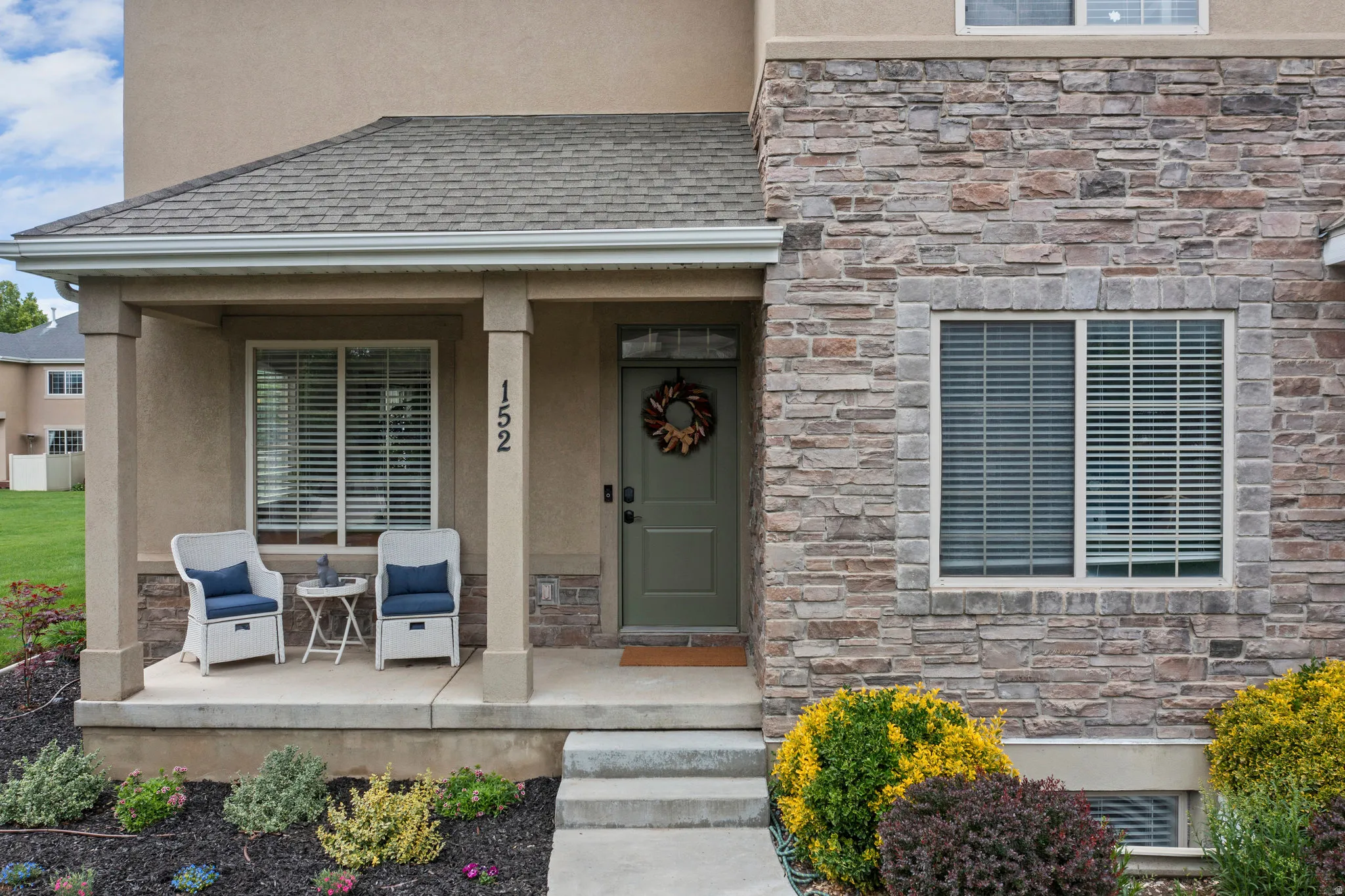 Doorway to property with stone siding, stucco siding, covered porch, and a shingled roof