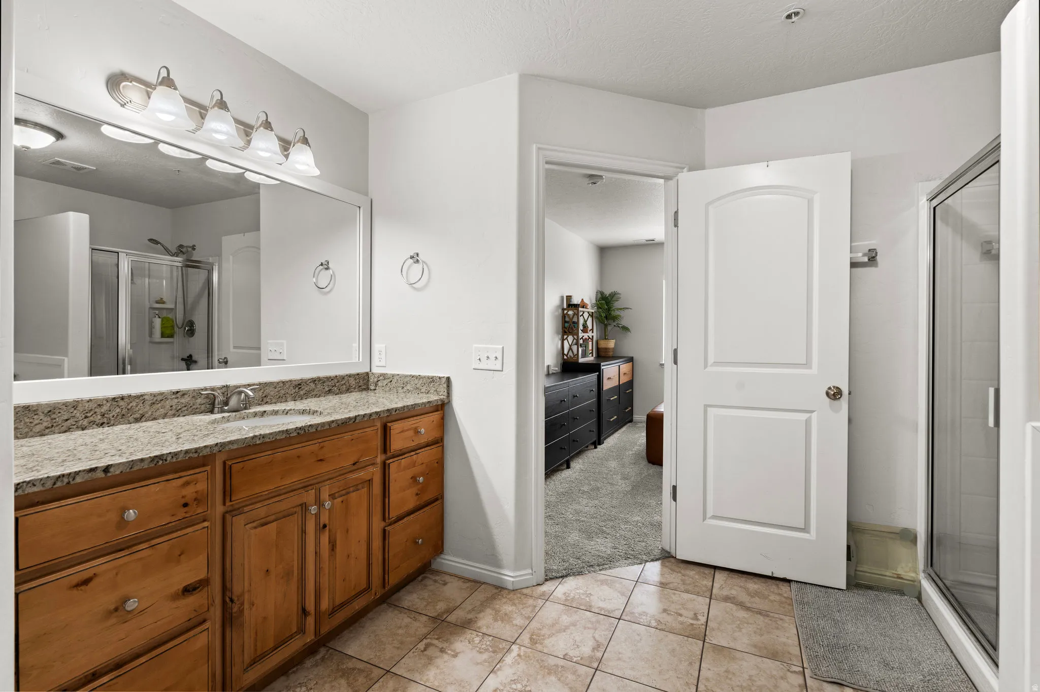 Bathroom featuring a shower stall, vanity, light tile patterned floors, connected bathroom, and a textured ceiling