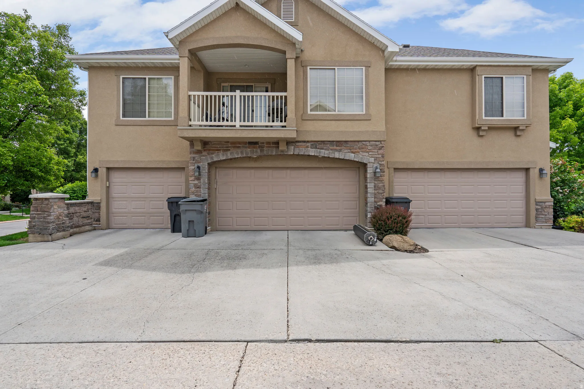 View of front facade featuring stone siding, a balcony, stucco siding, and a garage