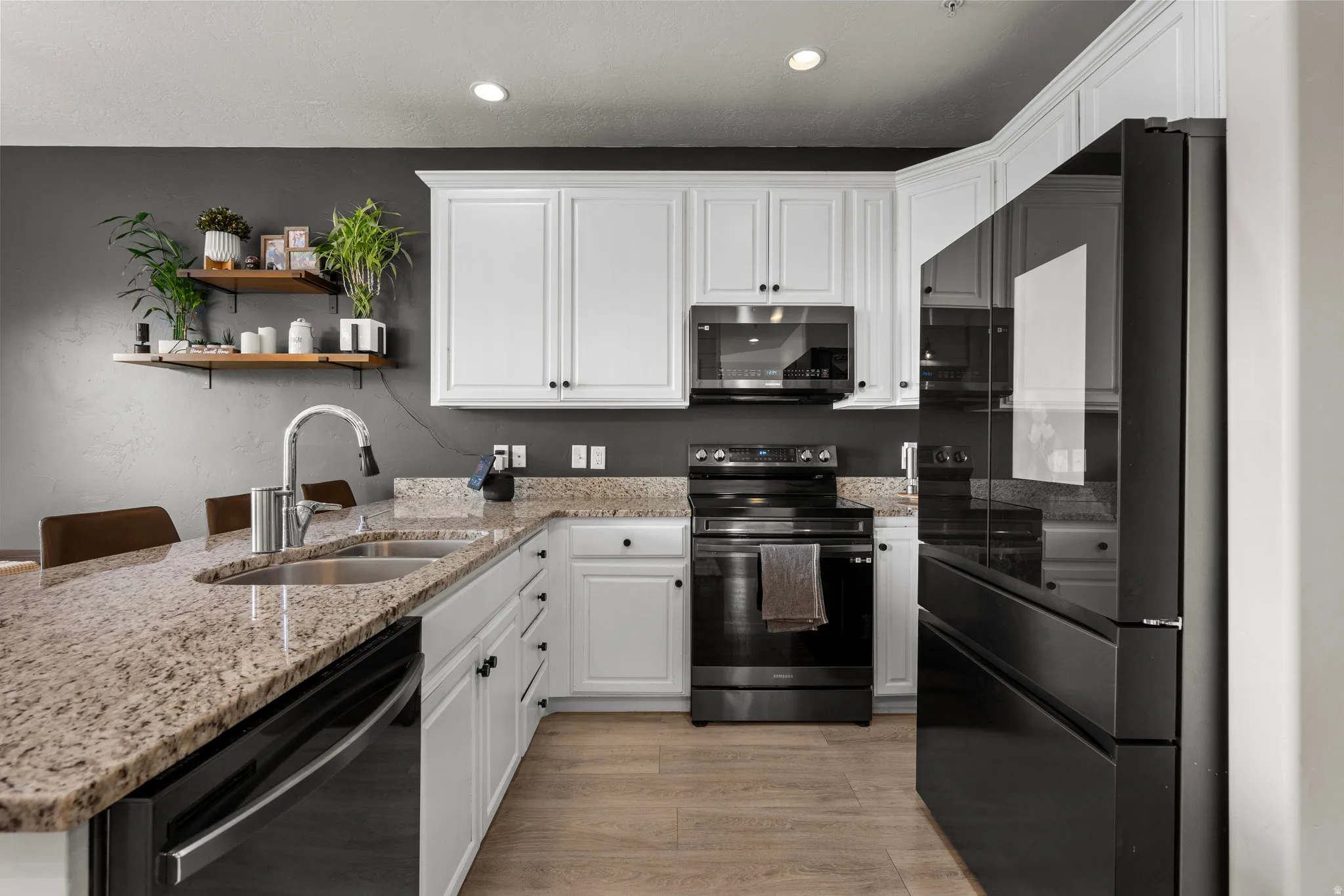 Kitchen featuring black appliances, light stone counters, white cabinetry, a peninsula, and open shelves