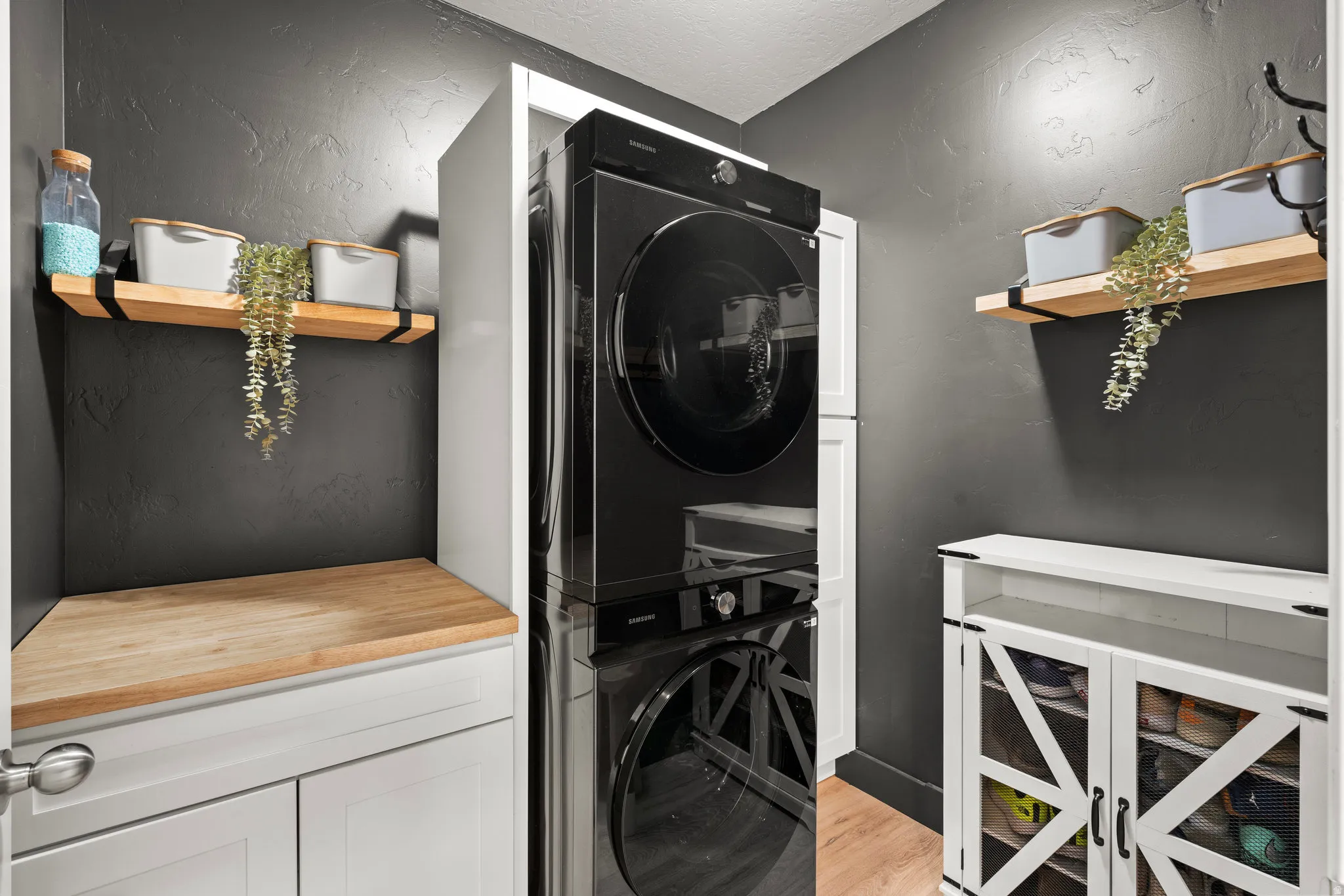 Laundry room with cabinet space, stacked washer / dryer, light wood-style flooring, and a textured wall