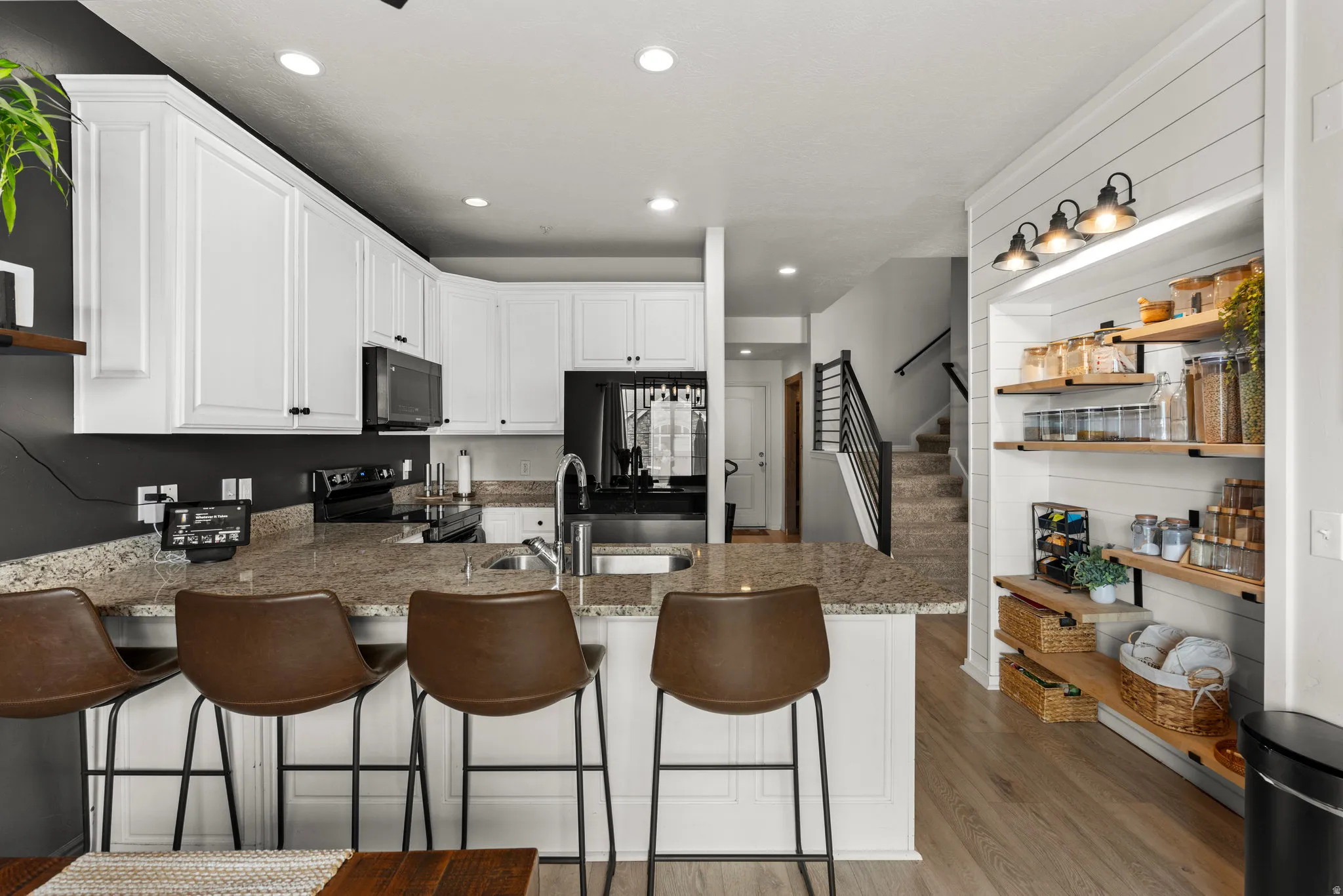 Kitchen with white cabinets, a peninsula, light wood-style floors, black appliances, and dark stone counters