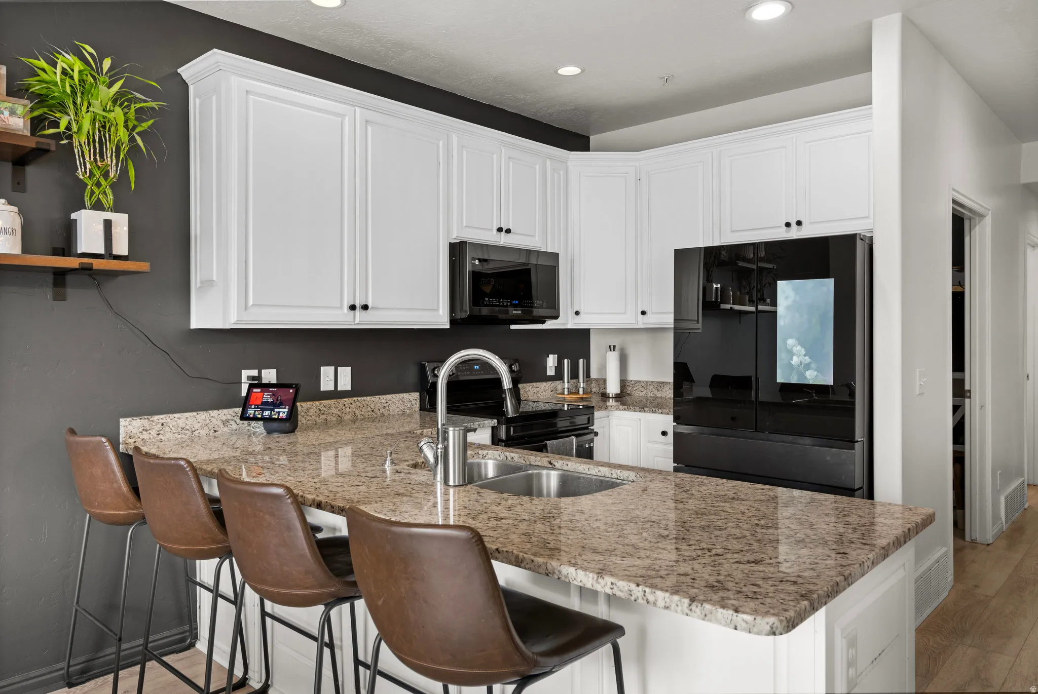 Kitchen with white cabinets, freestanding refrigerator, a peninsula, light stone counters, and light wood-style floors