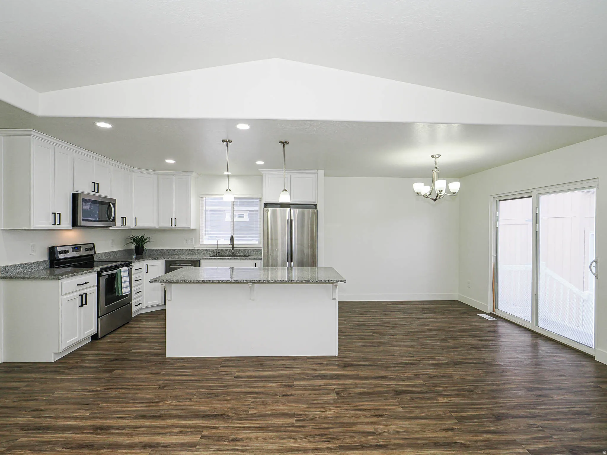 Kitchen with dark stone counters, stainless steel appliances, white cabinetry, a kitchen island, and dark wood-style floors