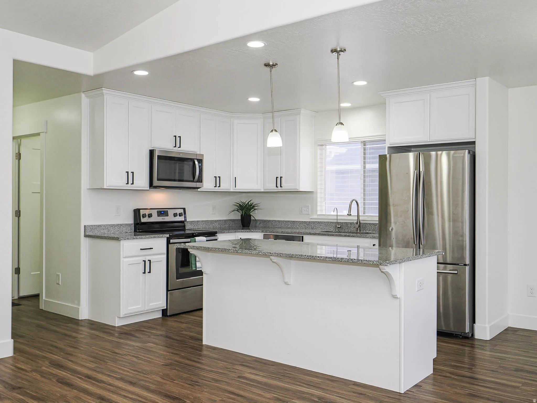 Kitchen featuring light stone countertops, stainless steel appliances, pendant lighting, and white cabinets