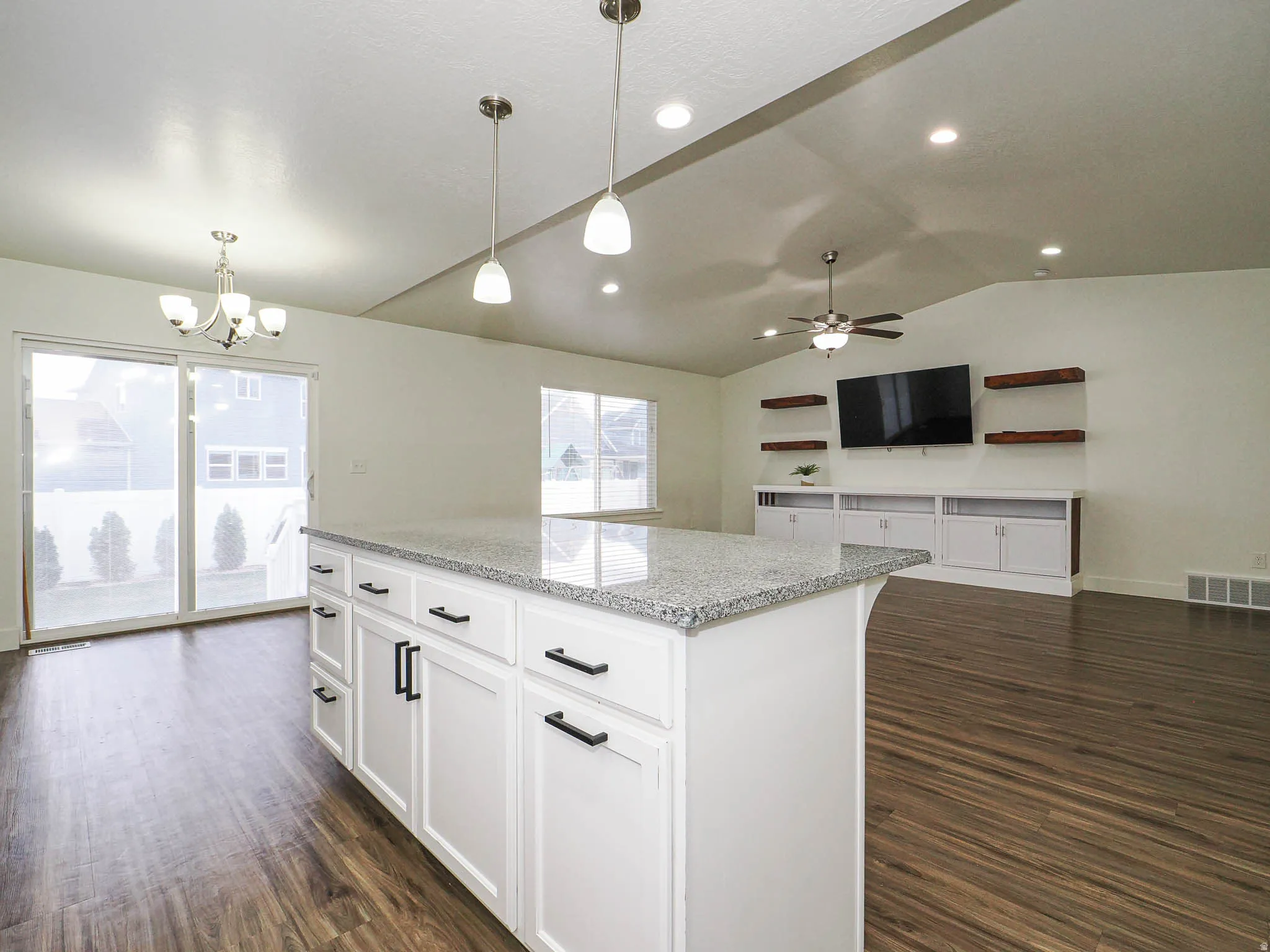 Kitchen featuring light stone counters, a kitchen island, white cabinetry, dark wood-type flooring, and a chandelier