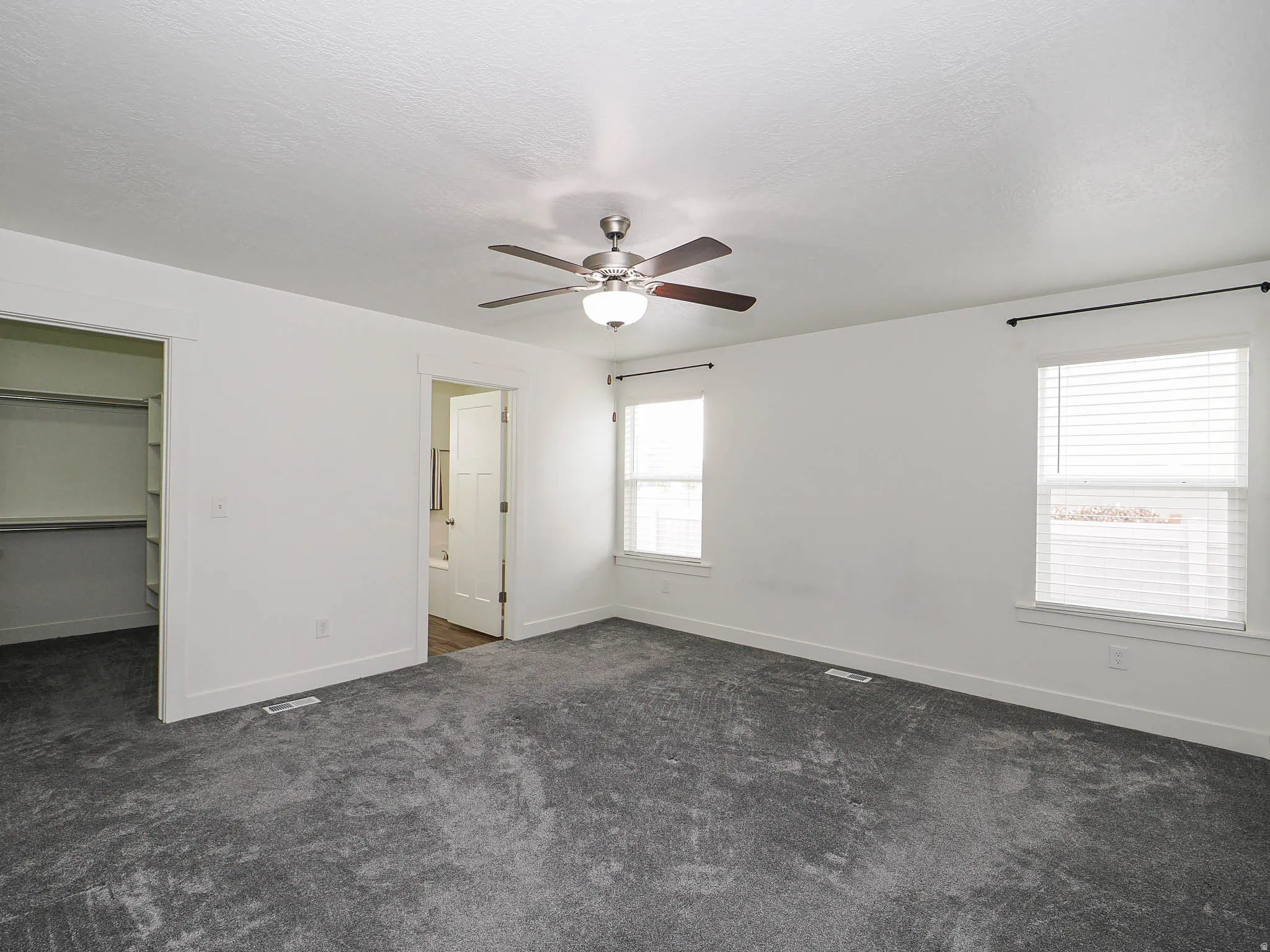 Unfurnished bedroom featuring dark colored carpet, a walk in closet, ceiling fan, a textured ceiling, and connected bathroom