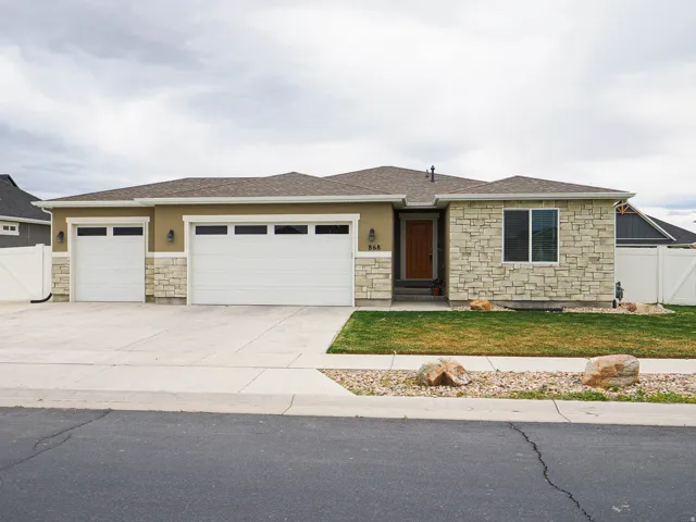 View of front of property with stone siding, driveway, an attached garage, and roof with shingles