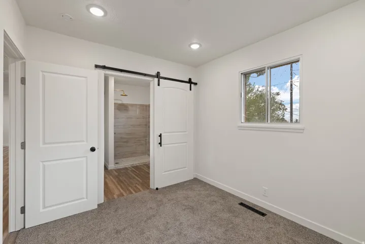 Unfurnished bedroom with connected bathroom, light colored carpet, and a barn door