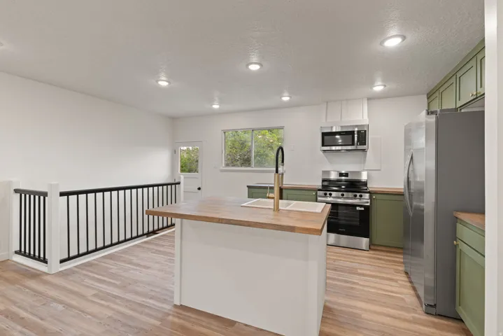 Kitchen with green cabinets, butcher block countertops, stainless steel appliances, light wood-style flooring, and recessed lighting