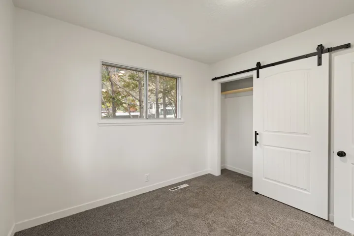 Unfurnished bedroom with a barn door, dark colored carpet, and a closet