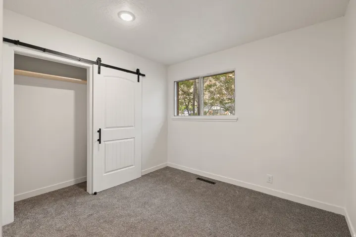 Unfurnished bedroom featuring a barn door, carpet, a closet, and a textured ceiling