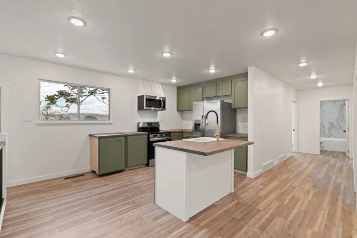 Kitchen with green cabinets, stainless steel appliances, light wood finished floors, a center island with sink, and butcher block counters