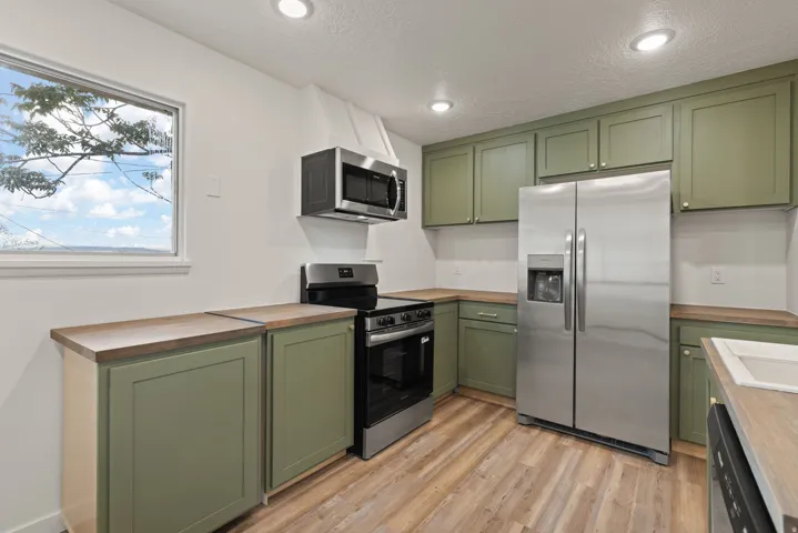 Kitchen featuring green cabinets, wooden counters, stainless steel appliances, light wood-style flooring, and recessed lighting