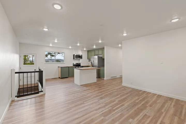 Kitchen featuring green cabinets, open floor plan, light wood-type flooring, stainless steel appliances, and a center island with sink