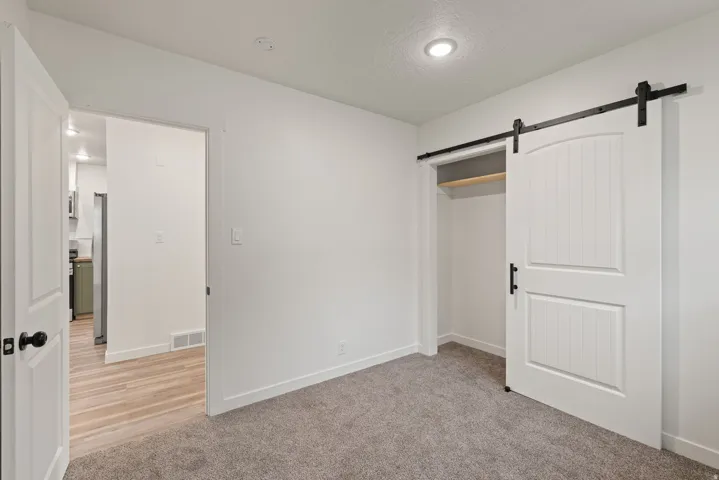 Unfurnished bedroom featuring a barn door, light colored carpet, a textured ceiling, a closet, and freestanding refrigerator