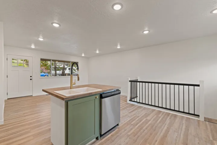 Kitchen with green cabinets, light wood-type flooring, dishwasher, a center island with sink, and recessed lighting