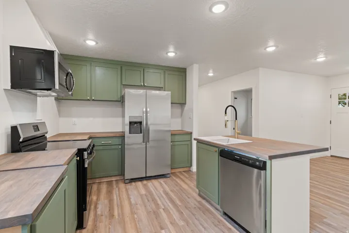 Kitchen with green cabinetry, stainless steel appliances, butcher block countertops, light wood finished floors, and recessed lighting