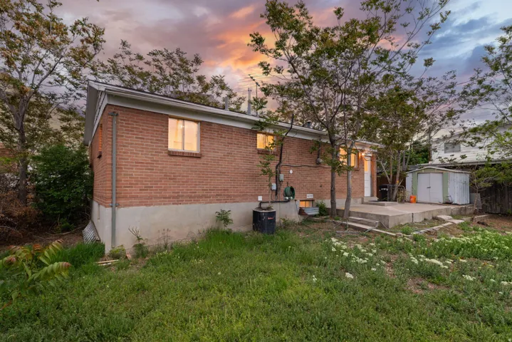 Back of house with a storage unit, brick siding, and a yard