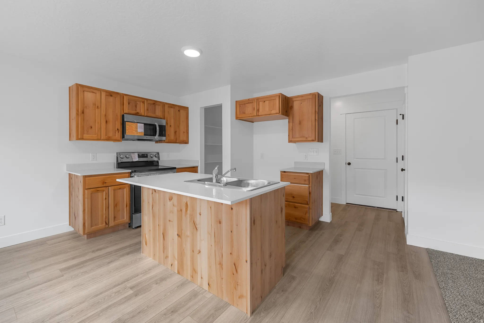 Kitchen with stainless steel appliances, a center island with sink, light wood finished floors, and wood finish cabinets