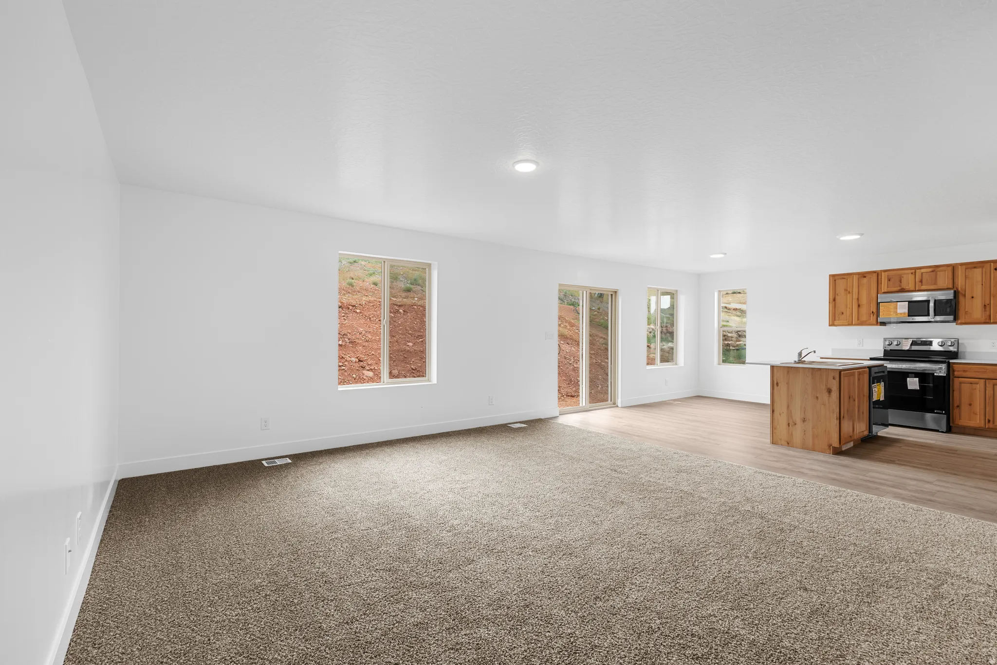 Kitchen featuring open floor plan, stainless steel appliances, light colored carpet, wood finish cabinetry, and light countertops