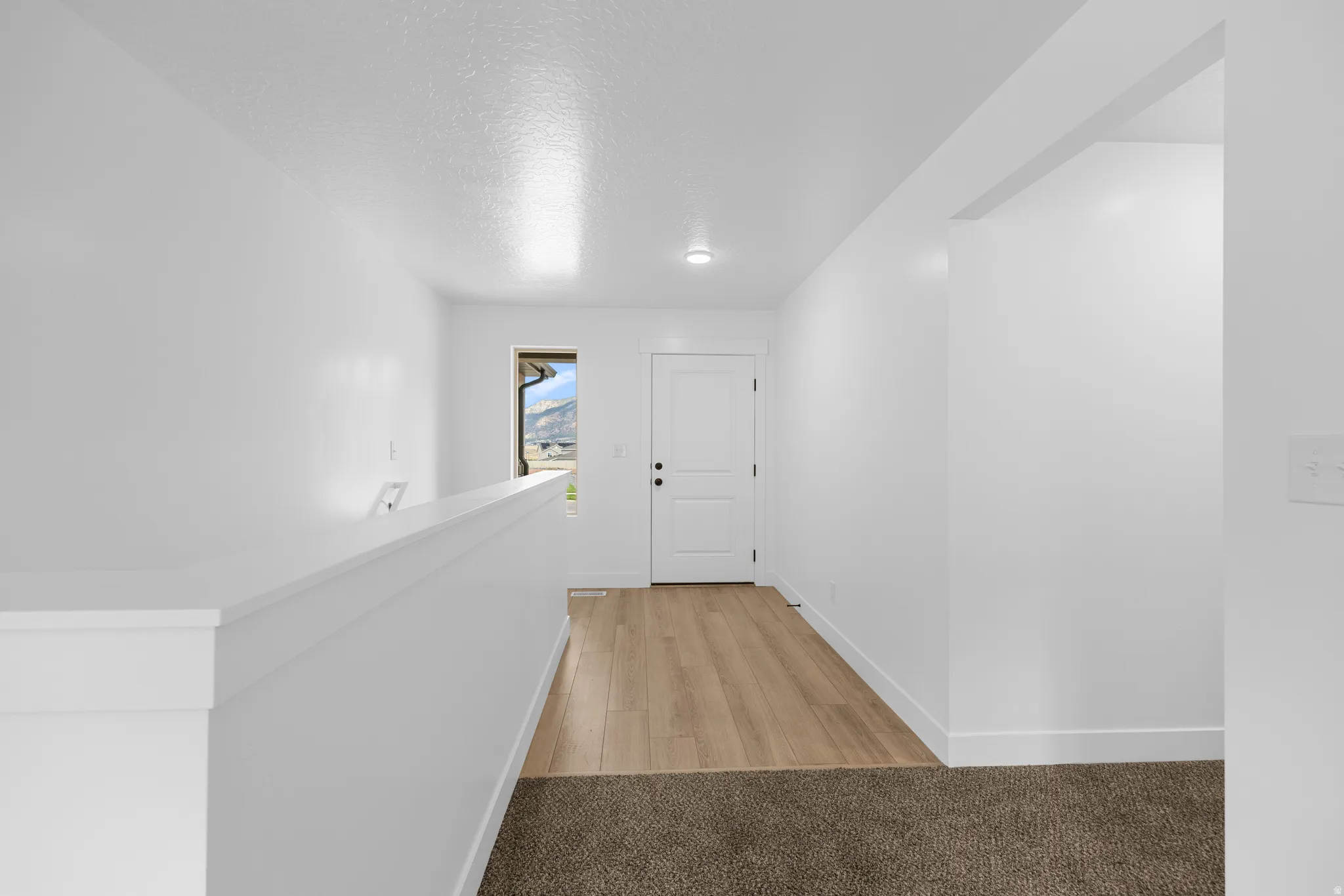 Hallway with light colored carpet and a textured ceiling