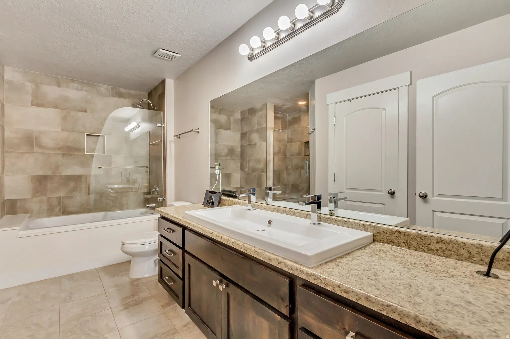 Full bath with vanity, tiled shower / bath, a textured ceiling, and light tile patterned flooring