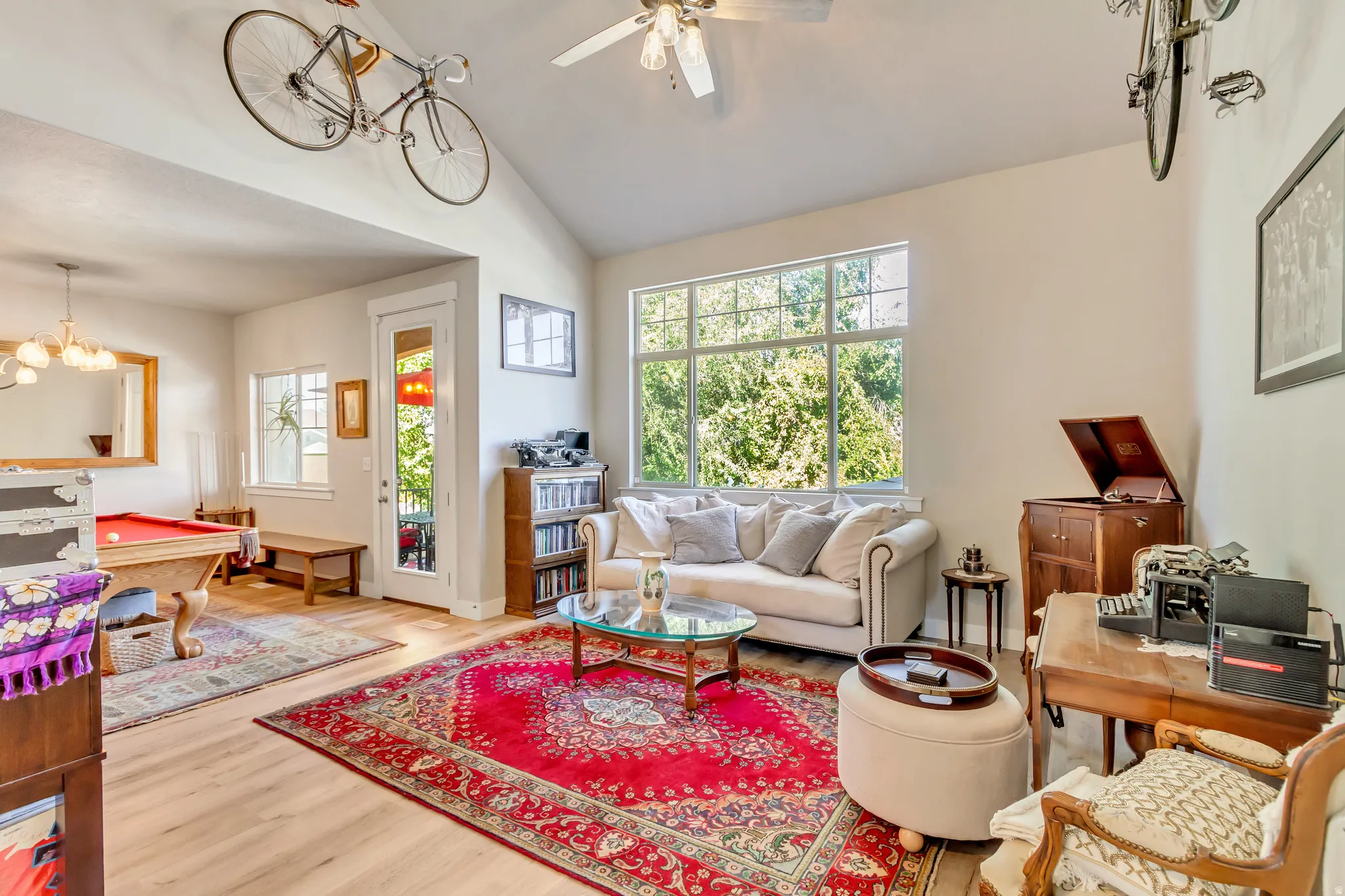 Living area with light wood finished floors, vaulted ceiling, ceiling fan, billiards table, and a chandelier