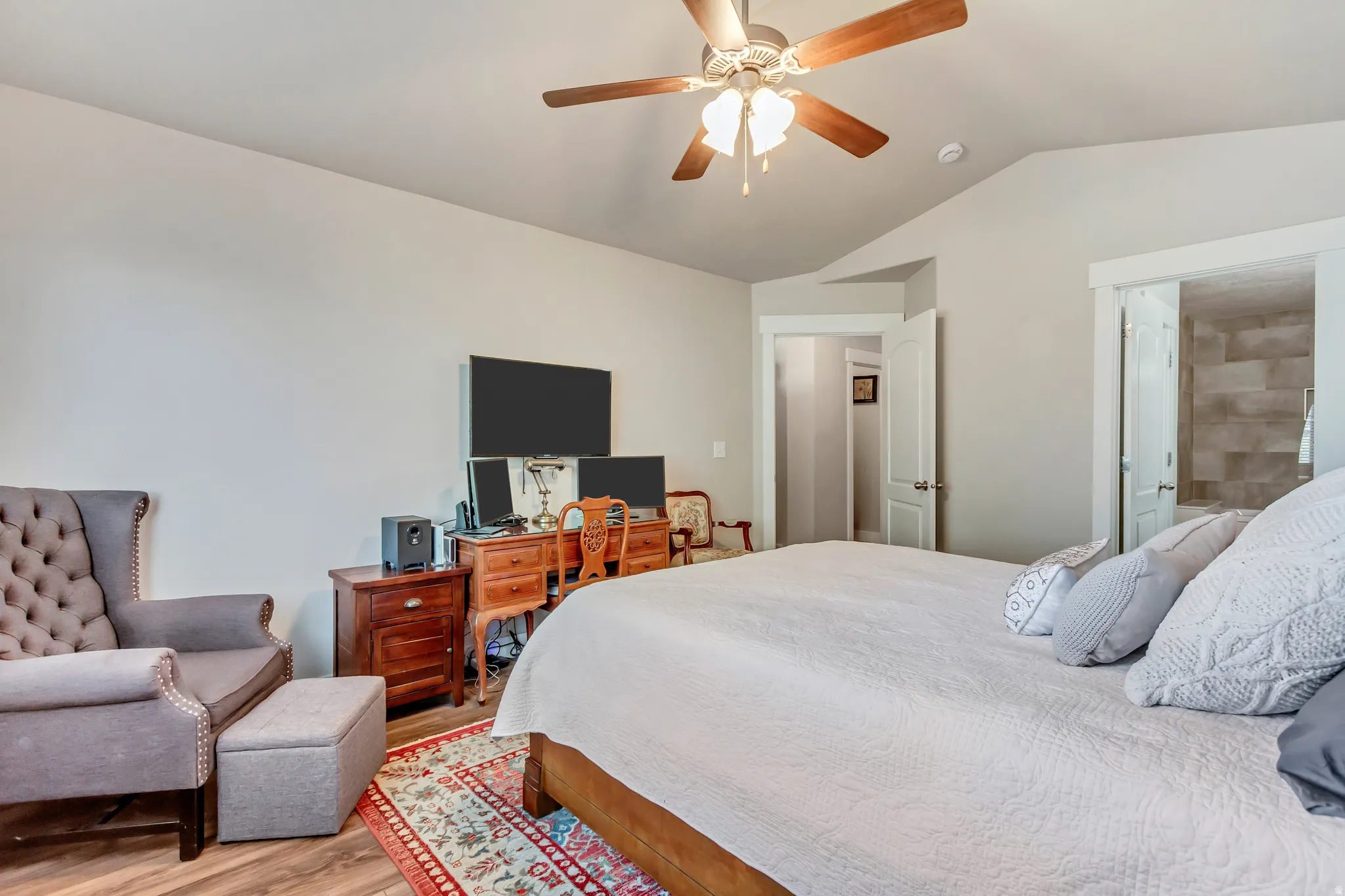 Bedroom with light wood-style floors, ceiling fan, and ensuite bath