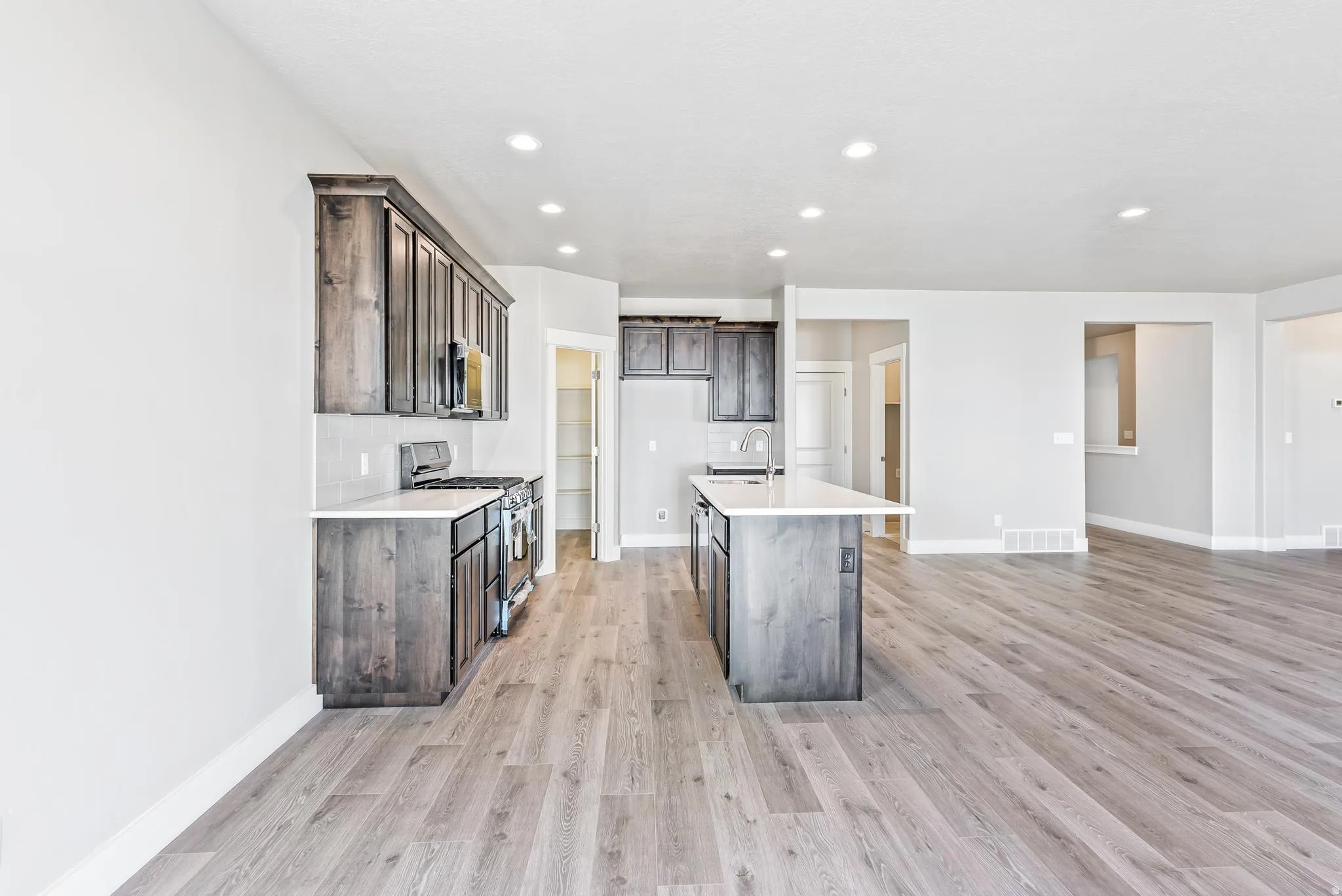 Kitchen featuring stainless steel gas range, dark wood finish cabinets, light wood-type flooring, an island with sink, and recessed lighting
