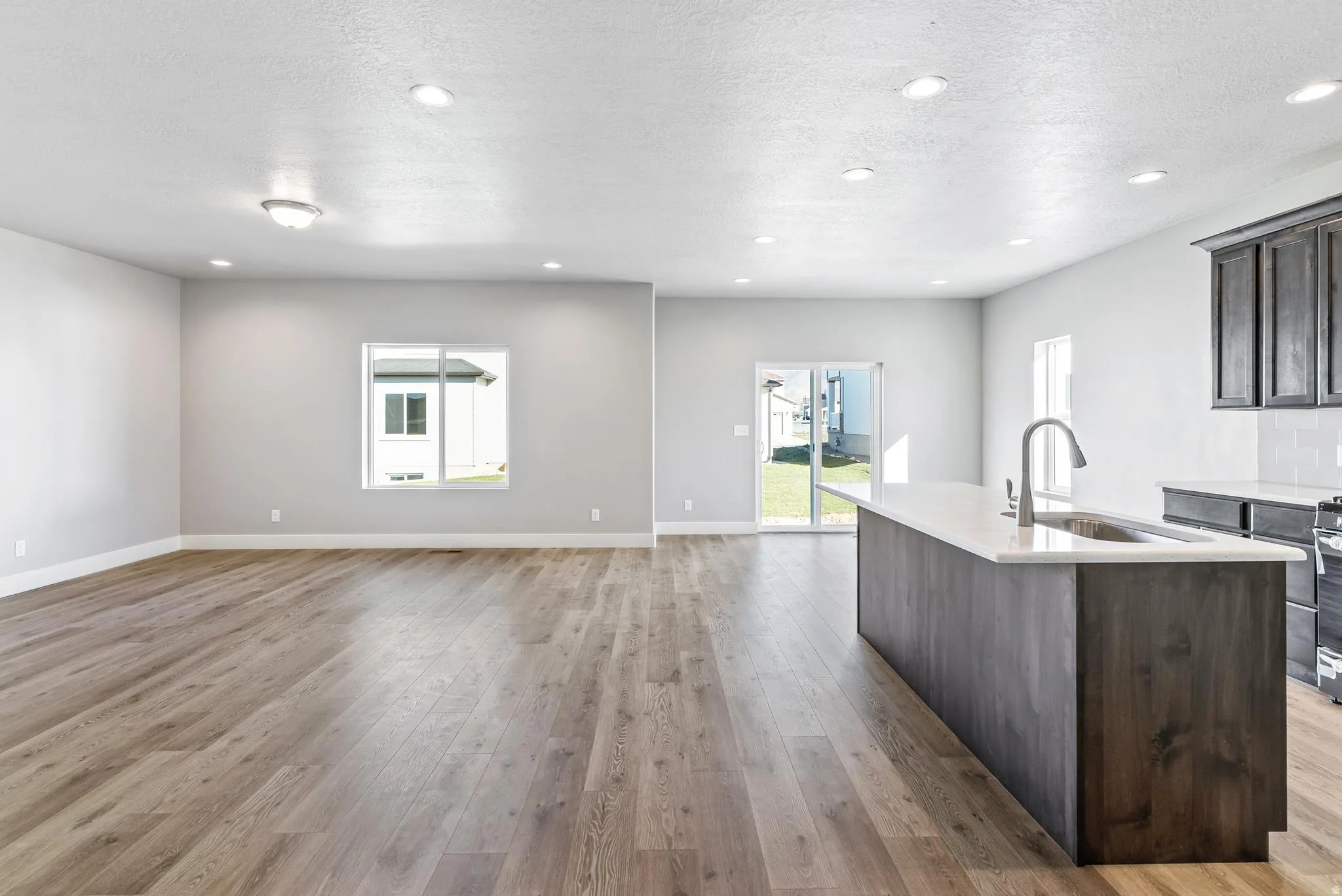 Kitchen featuring a center island with sink, dark wood finish cabinetry, light stone counters, light wood-type flooring, and open floor plan