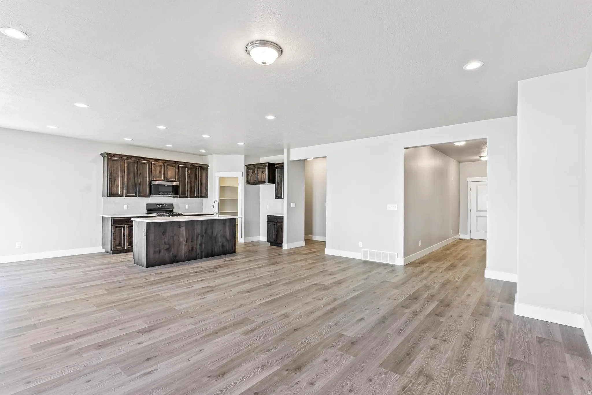 Kitchen featuring open floor plan, light countertops, dark wood finish cabinetry, a kitchen island with sink, and recessed lighting