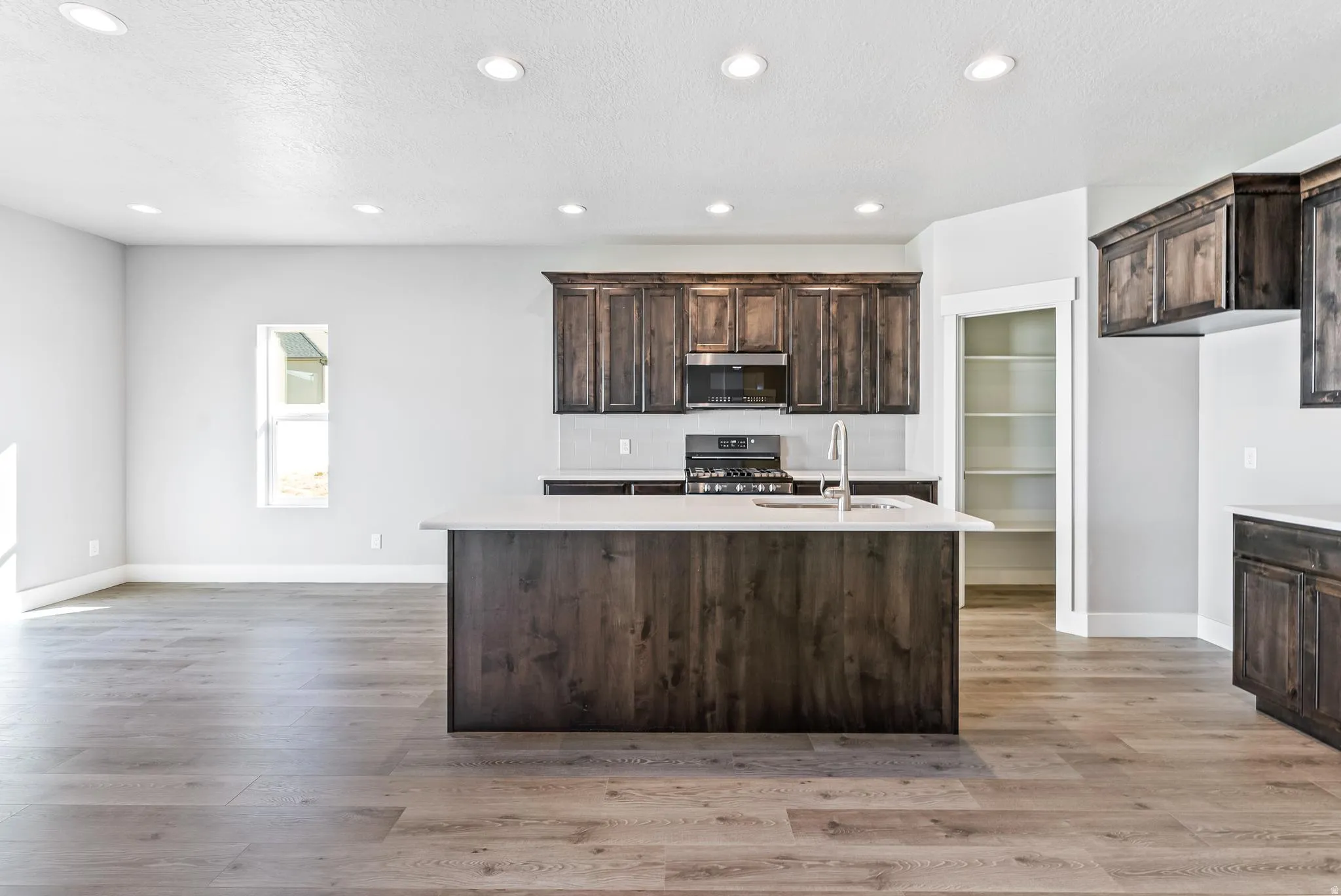 Kitchen featuring dark wood finish cabinets, a kitchen island with sink, black range with gas stovetop, recessed lighting, and light wood finished floors
