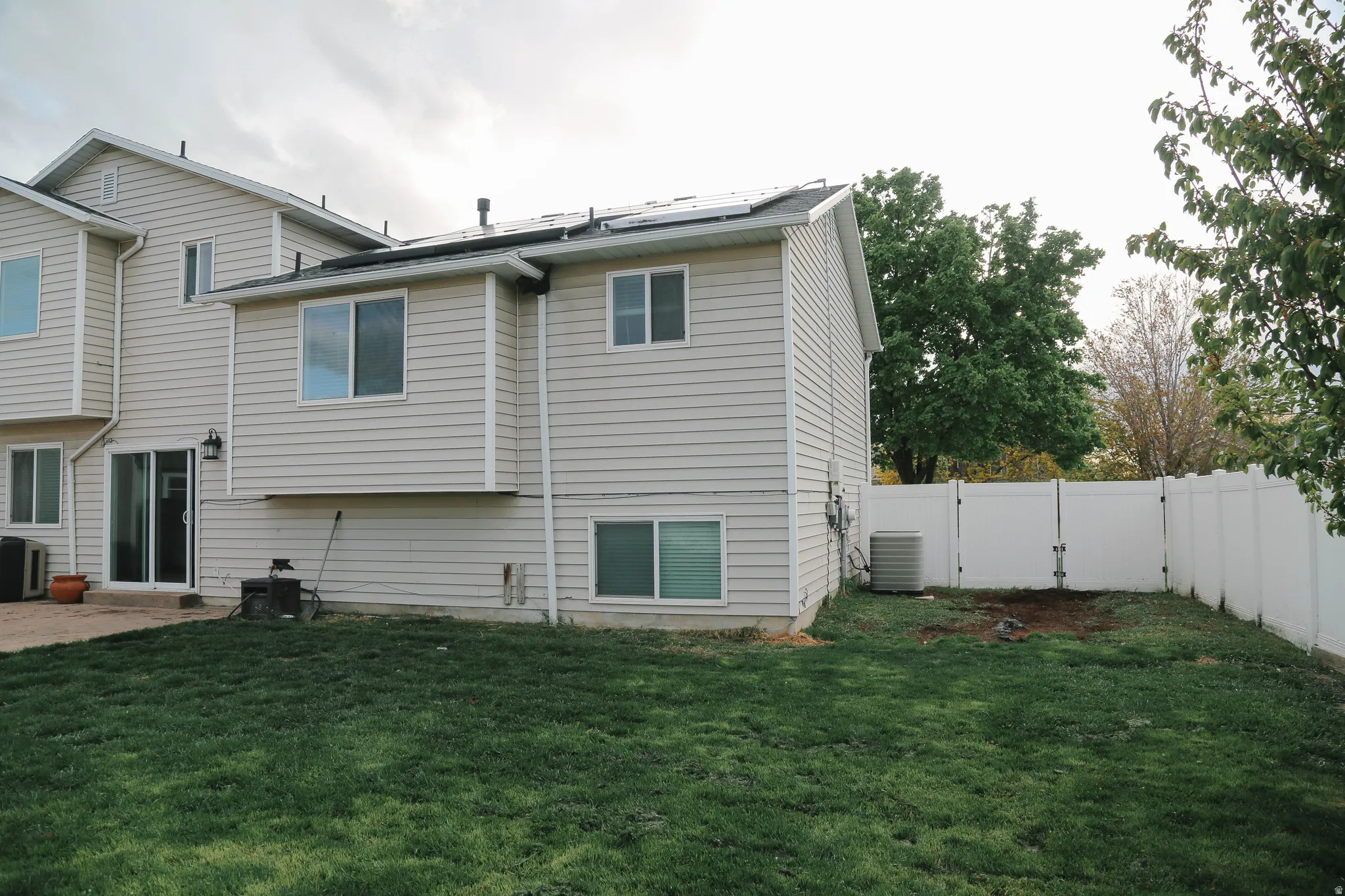 Back of property featuring roof mounted solar panels, a fenced backyard, a patio, and a gate