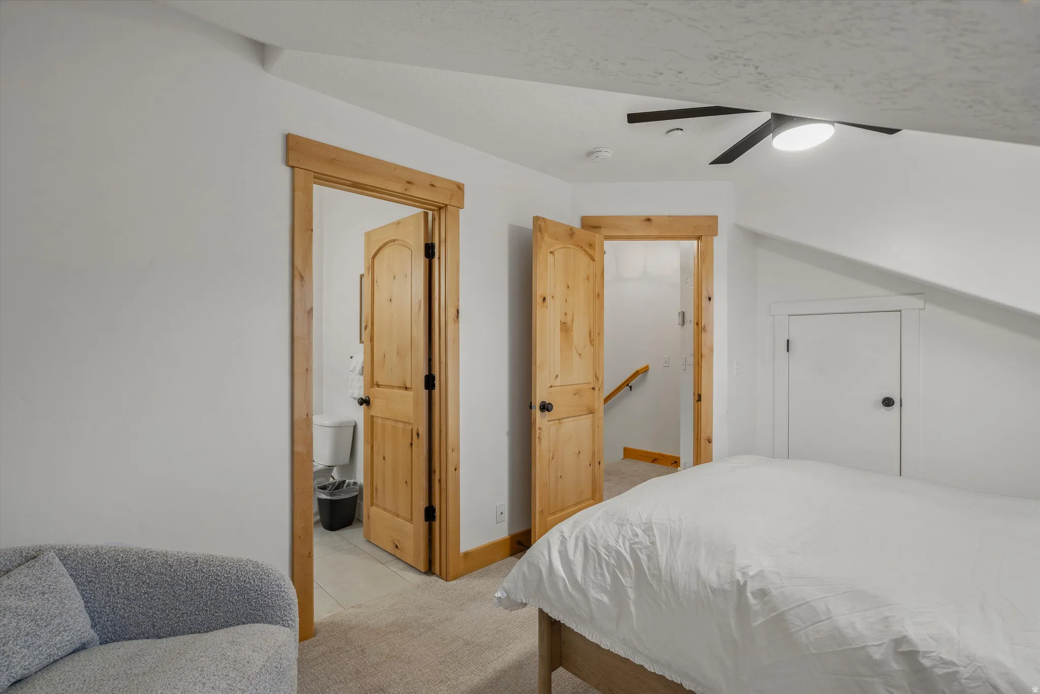 Bedroom with ceiling fan, light colored carpet, and ensuite bathroom