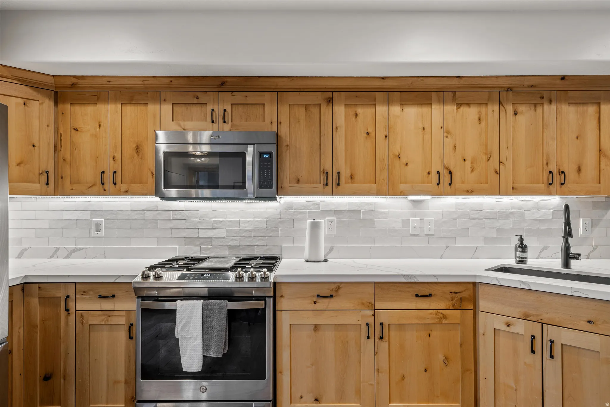 Kitchen featuring stainless steel appliances, decorative backsplash, and light wood finish cabinetry