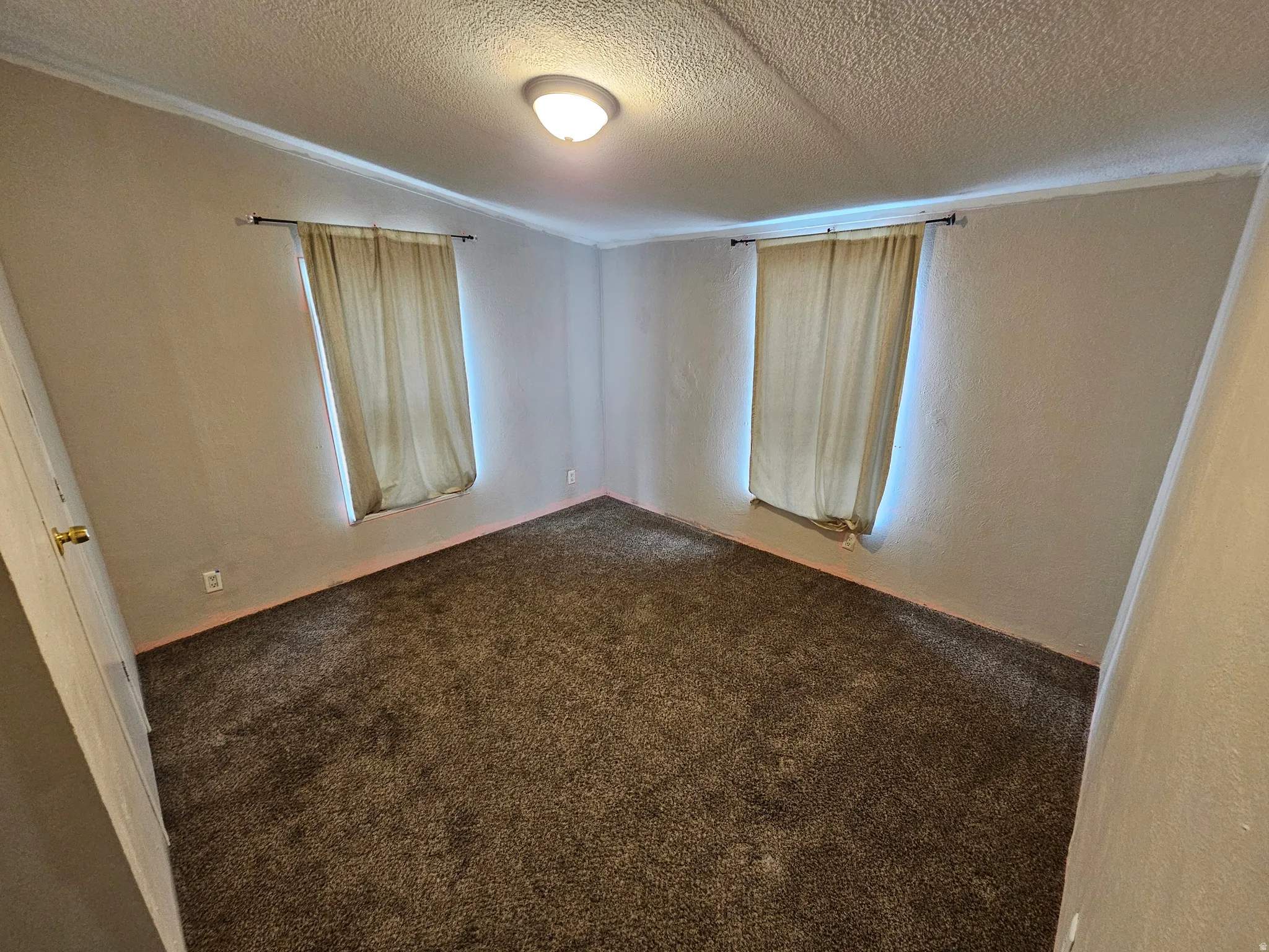Unfurnished room with dark colored carpet, a textured wall, and a textured ceiling
