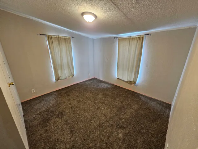 Unfurnished room with dark colored carpet, a textured wall, and a textured ceiling