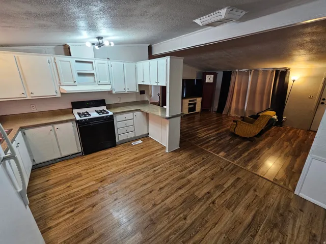 Kitchen featuring a textured ceiling, gas range, dark wood-style flooring, white cabinets, and cooling unit