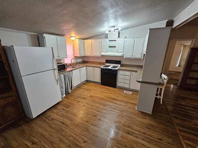 Kitchen featuring freestanding refrigerator, gas range, crown molding, a kitchen breakfast bar, and white cabinets