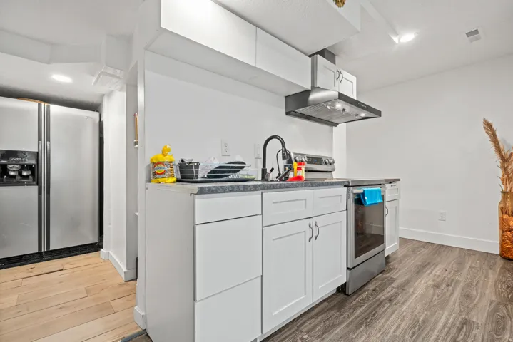 Kitchen featuring stainless steel appliances, white cabinetry, light wood-style flooring, dark countertops, and recessed lighting
