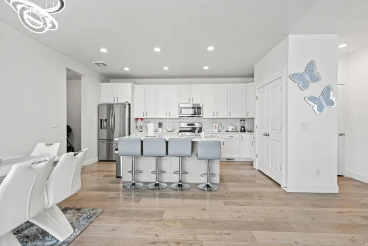 Kitchen with a kitchen breakfast bar, white cabinetry, a kitchen island with sink, stainless steel appliances, and light wood-type flooring