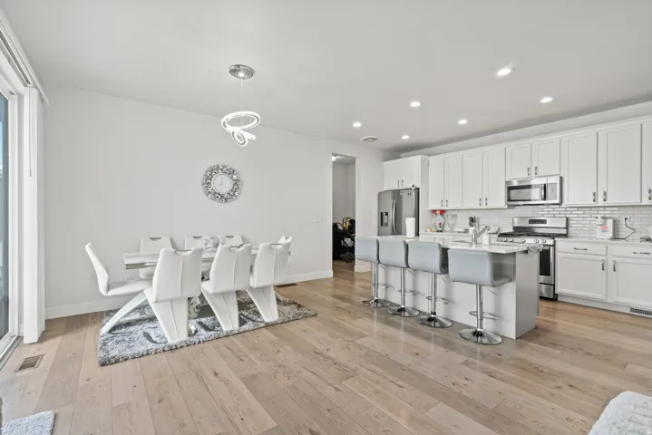 Kitchen with white cabinets, stainless steel appliances, a breakfast bar, a center island with sink, and hanging light fixtures
