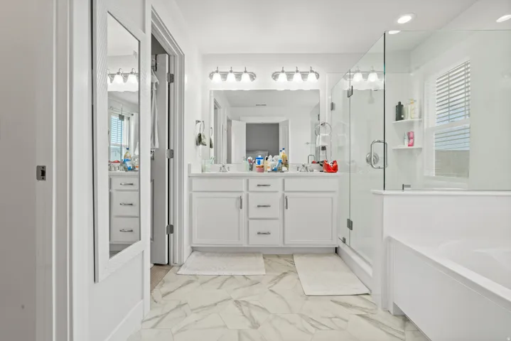 Full bath with double vanity, a stall shower, a bath, and healthy amount of natural light
