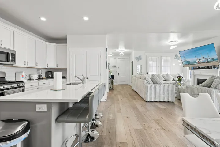 Kitchen featuring white cabinetry, light wood-style flooring, a breakfast bar, a fireplace, and a kitchen island with sink