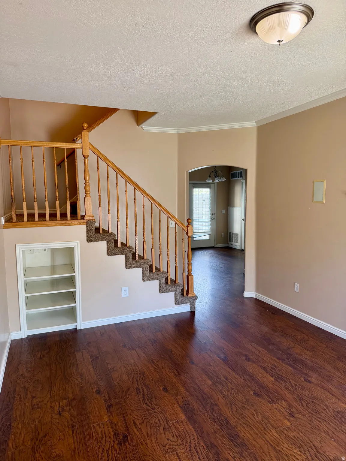 Unfurnished living room with arched walkways, dark wood-style floors, a textured ceiling, ornamental molding, and built in shelves